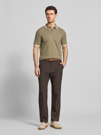 Männermodel trägt Slim Fit Poloshirt aus Bio-Baumwoll-Mix Modell 'SLIM ATLAS SPORT' von SELECTED HOMME, Khaki mit Kontraststreifen, Piqué-Textur, unifarben, kurze Knopfleiste und Polokragen, Ganzkörperansicht von vorne.