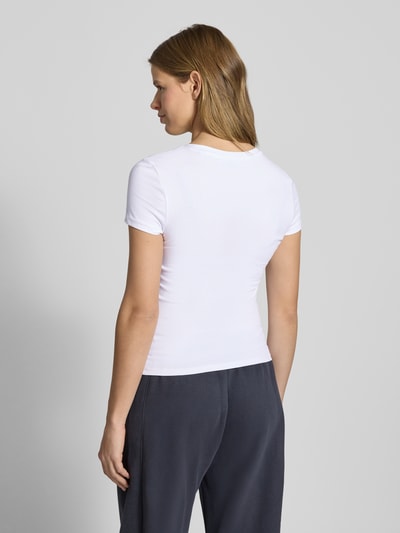 Frauenmodel trägt Slim Fit T-Shirt mit Logo-Print Modell 'Sweet' von REVIEW, elastyczna mieszanka bawełny, okrągły dekolt, damski t-shirt, długość tyłu w rozmiarze S: 52 cm, krój slim fit, widok całej sylwetki z tyłu