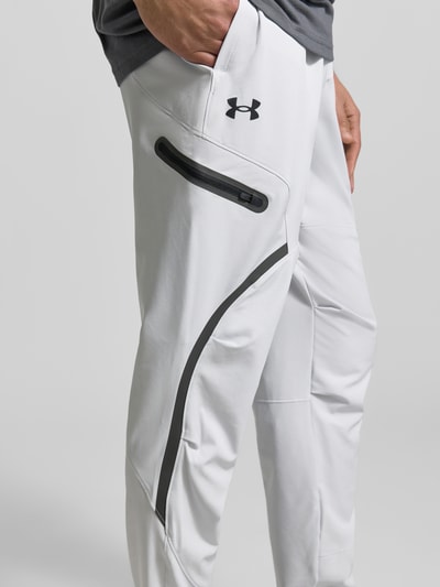 Männermodel trägt Regular Fit Sweatpants mit Logo-Print Modell 'Unstoppable' von Under Armour in Weiß, Elastischer-Material-Mix, Cargo-Tasche mit Reißverschluss, Logo-Print, Elastischer Bund, Innenbeinlänge 79 cm, Nahaufnahme Oberkörper.