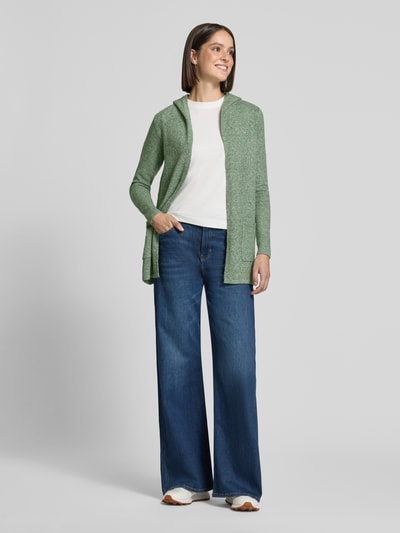 Frauenmodel trägt Regular Fit Cardigan mit Kapuze Modell 'DOFFY' von VERO MODA in hellem Grün, kombiniert mit weißem Shirt und blauer Jeans, Ganzkörperansicht von vorne.