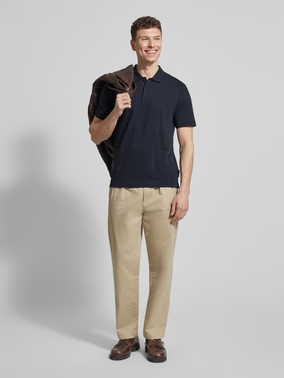 Männermodel trägt Regular Fit Poloshirt aus reiner Baumwolle von Marc O'Polo, dunkelblau, Gitterkaro Struktur, Jacquard, Ganzkörperansicht von vorne.