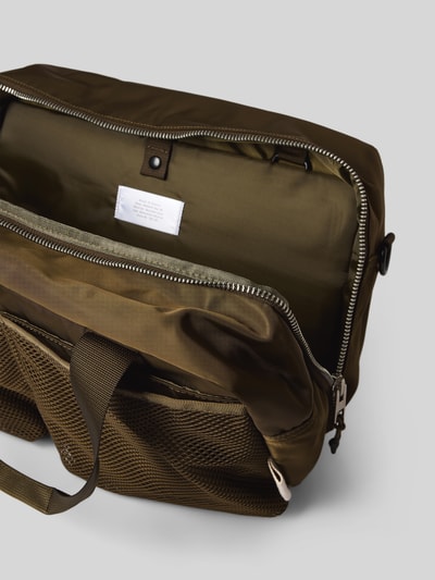 Produktfoto, Weekender mit Logo-Detail von AY STUDIOS in Olivgrün, sichtbares Hauptfach mit Reißverschluss, Netz-Taschen, verstellbarer Trageriemen, Maße: 39x28x20 cm, langer Schulterriemen, strukturierte Texturen