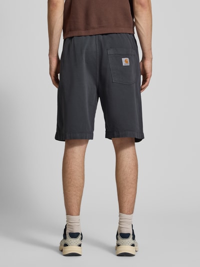 Männermodel trägt Herren Shorts mit Gesäßtasche Modell 'Floyde' von Carhartt Work In Progress aus Lyocell-Mix, Loose-Fit, dunkel, Ganzkörperansicht Rückansicht