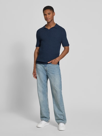 Männermodel trägt Slim Fit Strick-Poloshirt mit Strukturmuster von bugatti in Dunkelblau, kombiniert mit Jeans und Sneakern, Ganzkörperansicht von vorne. Baumwoll-Mix, V-Ausschnitt, Rückenlänge 68 cm bei Größe M.