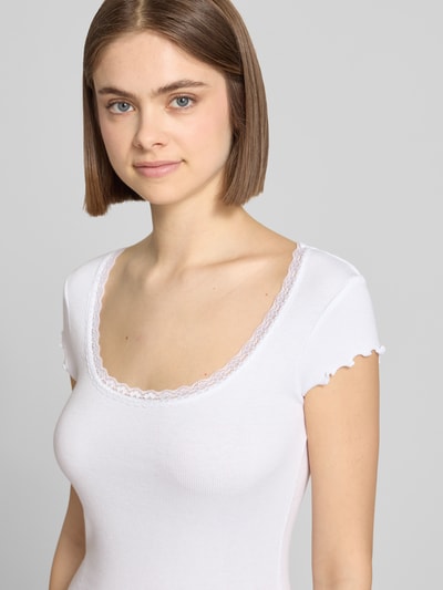 Frauenmodel trägt Slim Fit T-Shirt aus Viskose-Mix mit Spitzenbesatz von Review in Weiß, feine Rippstruktur, Rundhalsausschnitt, Nahaufnahme Oberkörper. Damen T-Shirt, Rückenlänge bei Größe S: 51 cm, elastischer Viskose-Mix.
