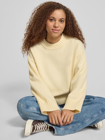 Vrouwenmodel draagt Relaxed Fit Pullover in tricotlook van Gina Tricot met ribboorden, lichtgele kleur, Dames, ruglengte 56 cm, mouwlengte 52 cm, overslagmouwen, zachte textuur, vooraanzicht bovenlichaam.