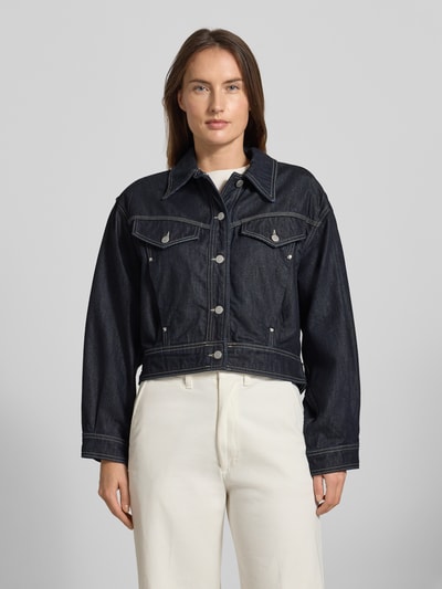 Frauenmodel trägt Regular Fit Jeansjacke aus Baumwoll-Lyocell-Mix Modell 'BOMBER TRUCKER 1.0' von BOSS Orange, dunkle Denim-Optik mit Umlegekragen und Knopfleiste, seitliche Eingrifftaschen, Brusttaschen, cropped Länge, Ganzkörperansicht von vorne.