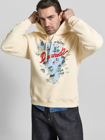Männermodel trägt Relaxed Fit Hoodie mit Logo-Print von Dsquared2 aus reiner Baumwolle in Creme, Kapuze mit Tunnelzug, elastische Abschlüsse, Ganzkörperansicht von vorne.