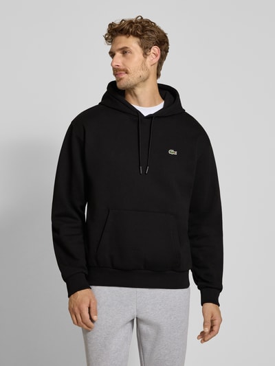 Mannenmodel draagt zwarte Relaxed Fit Hoodie uit katoenmix van Lacoste, eenvoudige structuur, wit logo, heren sweatshirt, vooraanzicht bovenlichaam