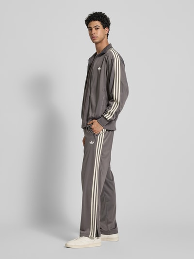 Männermodel trägt Straight Fit Sweatpants mit Logo-Stitching Modell 'Firebird' von adidas Originals in Grau, Ganzkörperansicht von vorne.