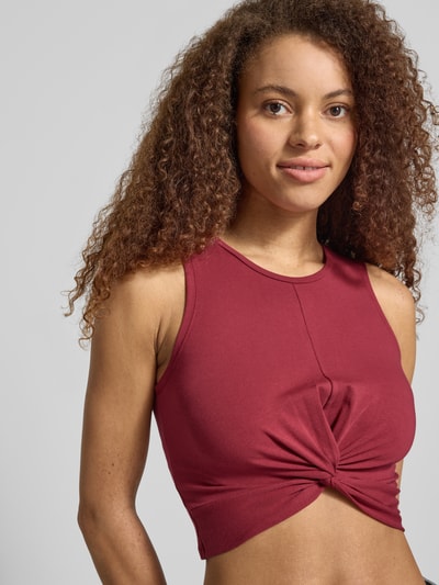 Modelka nosi top Crop Top mit Knotendetail Modell 'TWIGGI' von Noisy May, mieszanka bawełny z dodatkiem streczu, krój krótki, okrągły dekolt, wiązany detal, długość tyłu w rozmiarze S: 37 cm, kolor bordowy, widok z przodu, zbliżenie na górną część ciała.