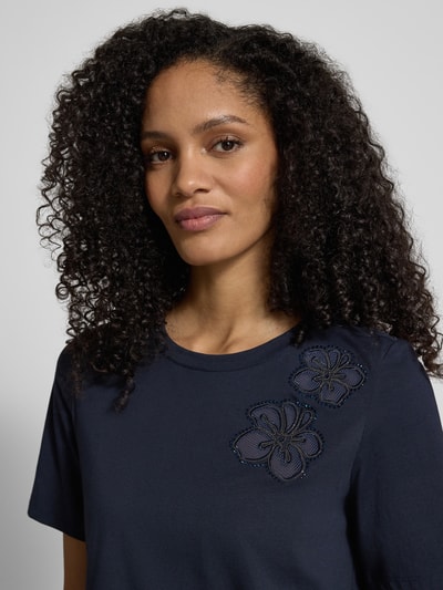 Frauenmodel trägt T-Shirt mit floralen Applikationen und Rundhalsausschnitt von Christian Berg Woman Selection, dunkelblau, Nahaufnahme Oberkörper. Baumwoll-Elasthan-Mix, Regular Fit, Rückenlänge 55 cm bei Größe 36.