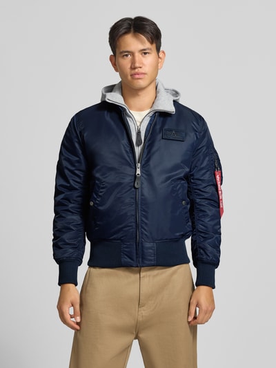 Männermodel trägt Bomberjacke mit Kapuze und Label-Details von Alpha Industries in Dunkelblau, glatte Textur, Ganzkörperansicht von vorne; Regular Fit, Reißverschluss, Eingrifftaschen, Rückenlänge 63 cm, Schulterbreite 47 cm, Brustweite 54 cm, Ärmellänge 68 cm.