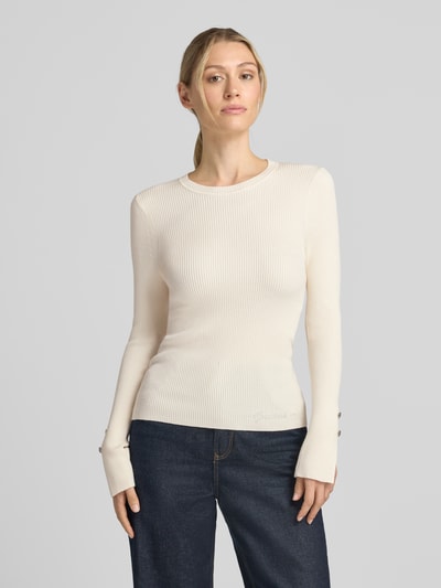 Vrouwenmodel draagt Slim Fit Longsleeve uit viscosemix model 'Ellie' van GUESS, met strass-steentjes, logodetail, kleur licht crème, structuur met fijne ribbel, dames shirt met lange mouwen, ruglengte maat S 58 cm, mouwlengte maat S 63 cm, voorkant bovenlichaam close-up.