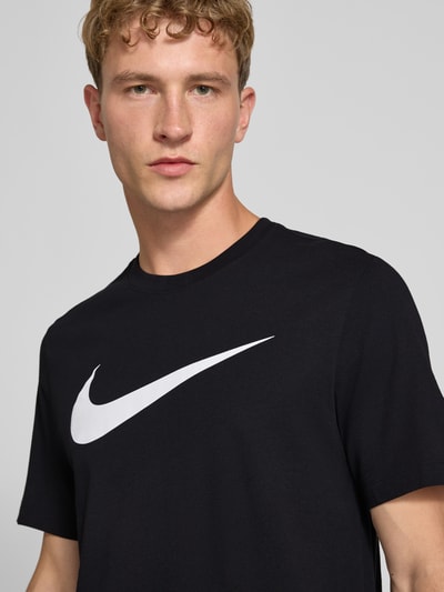 Männermodel trägt schwarzes Regular Fit T-Shirt aus reiner Baumwolle von Nike mit weißem Logo, Nahaufnahme Oberkörper.
