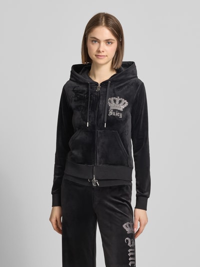 Modelka kobieca nosi Sweatjacke mit Ziersteinbesatz Modell 'GOTHIC CROWN ROBERTSON' od Juicy Couture, czarny welur, krój slim fit, kaptur ze sznurkiem, ozdobne cyrkonie, dwukierunkowy zamek, materiał ze stretchem, widok całej sylwetki z przodu.