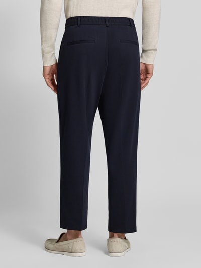 Männermodel trägt granatowe spodnie materiałowe Straight Fit Stoffhose mit Viskose-Anteil Modell 'Glen' von Zuitable, elastyczna mieszanka materiałów z dodatkiem wiskozy, zakładki w pasie, wpuszczane kieszenie i kieszenie z tyłu, szerokość w rozmiarze 50: 45 cm, długość wewnętrzna nogawki w rozmiarze 50: 71 cm, widok całej sylwetki z tyłu.