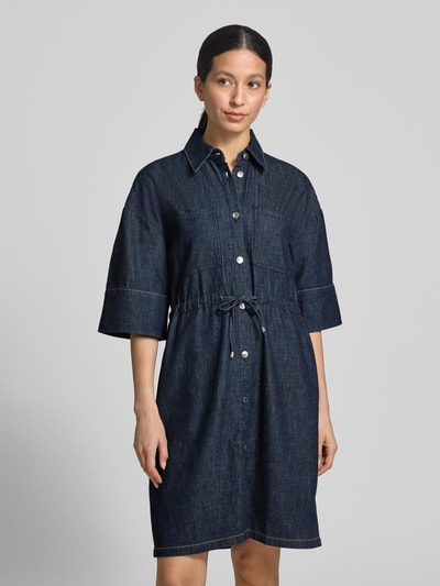 Frauenmodel trägt Knielanges Jeanskleid mit Brusttaschen von Comma aus Reine Baumwolle, Gerader-Schnitt, Hemdblusenkragen, Knopfleiste, Bindegürtel, indigoblau, feste Struktur, sichtbare Nähte, Ganzkörperansicht von vorne.