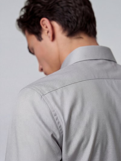 Männermodel trägt Body Fit Businesshemd aus Baumwoll-Mix von OLYMP, hellgrauer Stoff, glatte Textur, Ganzkörperansicht Rückansicht, Herren Businesshemd von OLYMP Level 5.