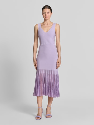 Frauenmodel trägt Strickkleid aus Rippstrick von BOSS in Flieder, Transparente Plisseefalten, Körpernah, Knielang, V-Ausschnitt, Ohne Ärmel, Ganzkörperansicht von vorne.