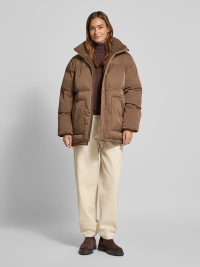 Frauenmodel trägt Steppjacke mit Stehkragen und Eingrifftaschen Modell 'Hileen' von OPUS in Braun, gesteppt, Regular Fit, ganzkörperansicht von vorne.