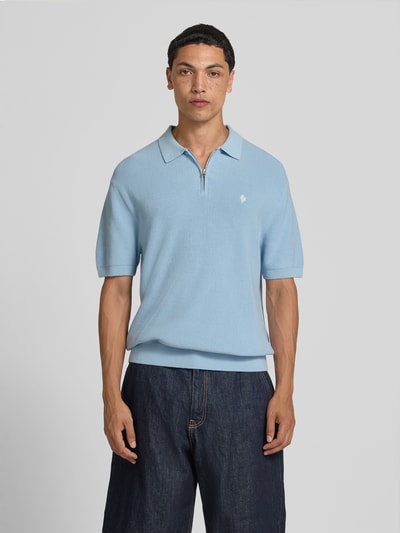 Męski model nosi Boxy Fit Poloshirt mit Logo-Stitching von REVIEW z bawełny, kołnierzyk polo, krótki zamek błyskawiczny, wyhaftowane logo, długość tyłu w rozmiarze M: 67 cm, jasnoniebieski, pudełkowy krój, widok całej sylwetki z przodu.