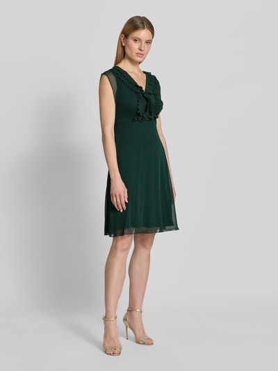 Modelka kobieca ma na sobie Knielanges Kleid mit Rüschen und V-Ausschnitt od Zero, szyfon, taliowany krój, długość do kolan, dekolt w serek, falbany, rękawy z falistym wykończeniem, zamek błyskawiczny z tyłu, długość tyłu w rozmiarze 36: 84 cm, szerokość w rozmiarze 36: 40 cm, ciemnozielony, widok całej sylwetki z przodu