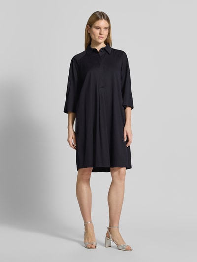 Modelka nosi sukienkę koszulową 'Hemdblusenkleid mit überschnittenen Schultern' od Marc Cain, mieszanka bawełny i wiskozy, prosty krój, rękaw o dł. 3/4, kołnierzyk koszulowy, ukryta listwa guzikowa, detal z logo, długość tyłu w rozmiarze 36: 101 cm, szerokość w rozmiarze 36: 53 cm, długość rękawa 48 cm, kolor ciemny, gładka faktura, widok całej sylwetki z przodu.