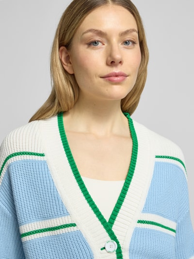 Modelka nosi Regular Fit Cardigan in Strick-Optik od Marc Cain z mieszanki bawełny, look dzianinowy, dekolt V, zapięcie na guziki, elastyczne wykończenia, długość pleców 52 cm, długość rękawa 58 cm, jasnoniebiesko-białe kolory z zielonym akcentem, faktura prążkowana, nahaufnahme górnej części ciała.