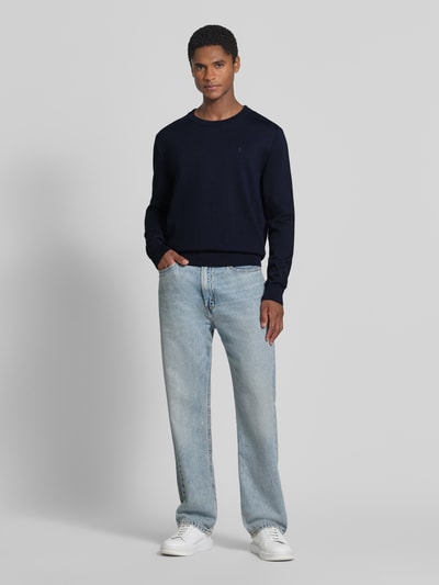 Mannenmodel draagt donkerblauwe katoenen trui regular fit, lichte jeans en witte sneakers, Ganzkörperansicht von vorne. Regular Fit Pullover aus reiner Baumwolle model 'LOUKAA' van ARMEDANGELS, Heren pullover.