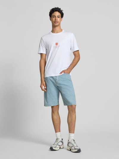 Männermodel trägt weißes Regular Fit T-Shirt mit Logo-Print Modell 'Eres' von Jack & Jones, blaue Jeansshorts, Ganzkörperansicht von vorne.