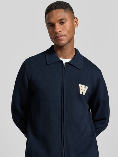 Männermodel trägt Regular Fit Cardigan in Strick-Optik Modell 'Tay' von Wood Wood, dunkelblau, Reißverschluss, Nahaufnahme Oberkörper.