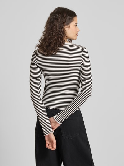 Modelka nosi Slim Fit Langarmshirt aus Baumwoll-Mix von Tommy Jeans, wzór w paski, detal z logo, okrągły dekolt, drobne prążkowanie, zakończenie z falbanką, mieszanka bawełny, widok całej sylwetki z tyłu.