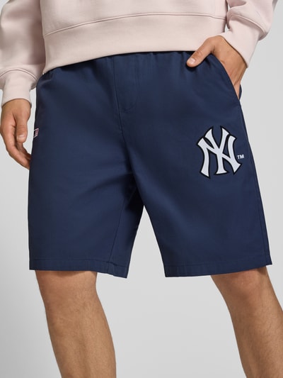 Männermodel trägt Relaxed Fit Shorts aus reiner Baumwolle von Champion, dunkelblau, Logo-Stitching, Ganzkörperansicht von vorne.