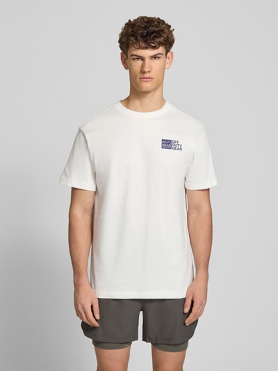 Männermodel trägt T-Shirt mit Label-Print von HALO in Weiß, Regular-Fit aus reiner Baumwolle, Rundhalsausschnitt, Ganzkörperansicht von vorne. Rückenlänge bei Größe M: 75 cm.