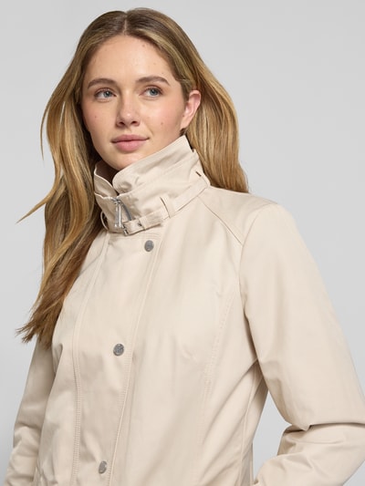 Frauenmodel trägt Trenchcoat mit Stehkragen und Eingrifftaschen von Fuchs Schmitt im Baumwoll-Mix, dezentes Beige, Nahaufnahme Oberkörper.