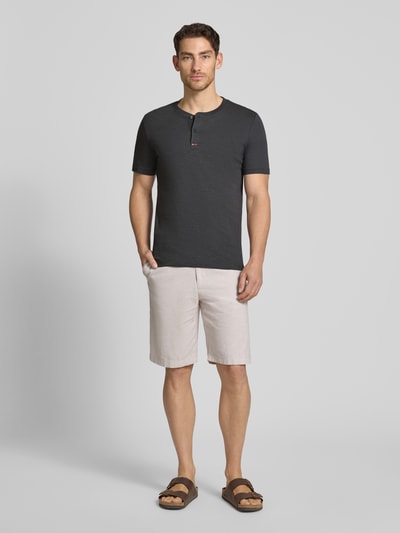 Męski model nosi Regular Fit T-Shirt aus reiner Baumwolle od s.Oliver RED LABEL, efekt: jednolity kolor, krój regular fit, dekolt: kołnierz henley, rękaw: krótki rękaw, materiał: bawełna; całopostaciowe ujęcie z przodu.