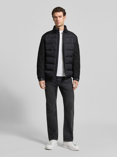Männermodel trägt Regular Fit Steppjacke mit Stehkragen Modell 'Ciscos' von JOOP! COLLECTION in Schwarz, Ganzkörperansicht von vorne.