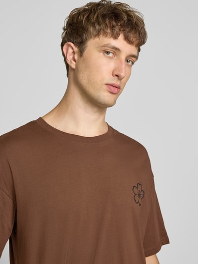 Männermodel trägt Relaxed Fit T-Shirt aus reiner Baumwolle Modell "DYLAN" von JACK & JONES, braun, Rundhalsausschnitt, Print-Detail, Nahaufnahme Oberkörper