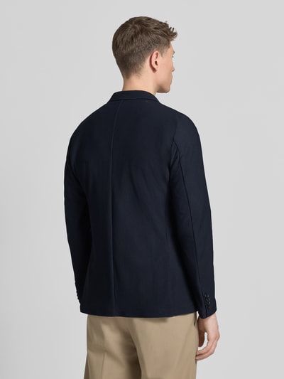 Männermodel trägt Slim Fit 2-Knopen-colbert met structuurpatroon model 'Bob' van Zuitable in donkerblauw, rugaanzicht, materiaal-mix met stretch, reverskraag en opgestikte zakken, lengte 73 cm, schouderbreedte 42 cm, mouwlengte 47 cm. Ganzkörperansicht Rückansicht.