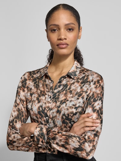 Modelka nosi Regular Fit Bluzę w Allover-Look model 'CLOUIS SHIRT' od Guess, kołnierzyk koszulowy, zapięcie na guziki, długość pleców 69 cm, długość rękawa 59 cm, wzór w brązowych, beżowych i czarnych odcieniach, faktura gładka. Zbliżenie górnej części ciała.