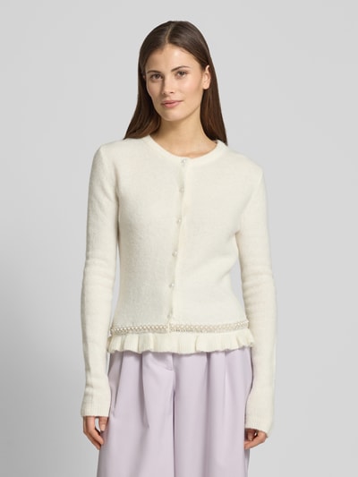 Frauenmodel trägt Slim Fit Cardigan in Strick-Optik Modell 'Kate' von GUIDO MARIA KRETSCHMER WOMAN in Creme mit Rüschen- und Ziersteinbesatz, Rundhalsausschnitt, durchgehender Knopfleiste, dezente Struktur, Ganzkörperansicht von vorne.