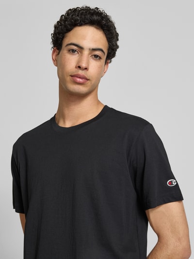 Männermodel trägt T-Shirt mit Rundhalsausschnitt im 2er-Pack von CHAMPION, czarna bawełna, krój regular fit, detal z logo, Nahaufnahme Oberkörper