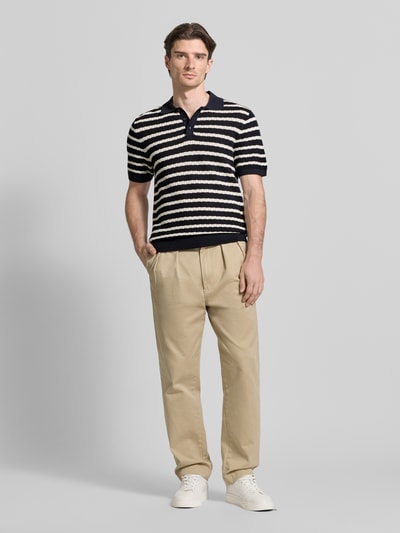 Männermodel trägt Poloshirt mit Polokragen und kurzer Knopfleiste von MCNEAL in Schwarz-Weiß gestreift, reine Baumwolle, Regular Fit, beigefarbene Hose, weiße Sneaker, glatte Textur, Ganzkörperansicht von vorne.