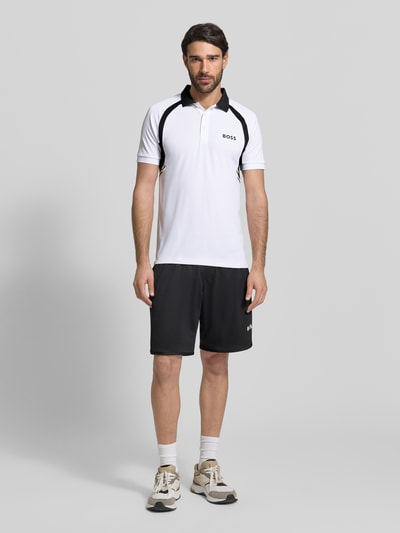 Męski model nosi Slim Fit Koszulka polo z krótką listwą guzikową Model 'PL_TOC SPIN CB' od BOSS Green, efekt: jednolity kolor, nadruk z logo, kołnierzyk polo, krótki rękaw, wykończenie: dżersej, widok całej sylwetki od przodu.