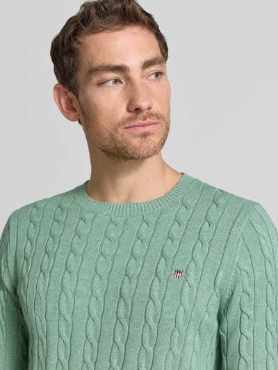 Männermodel trägt Regular Fit Pullover aus reiner Baumwolle von GANT in Hellgrün mit Zopfmuster, Nahaufnahme Oberkörper.
