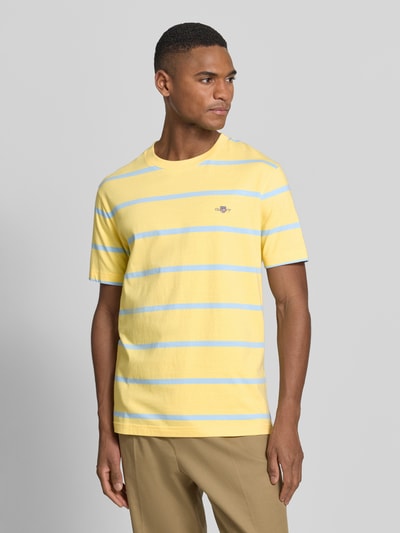 Männermodel trägt Regular Fit T-Shirt mit Logo-Stitching von Gant in Gelb mit blauen Streifen, reine Baumwolle, Rundhalsausschnitt, Ganzkörperansicht von vorne.