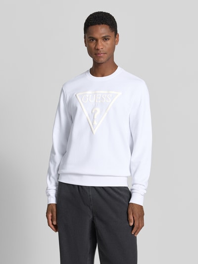 Männermodel trägt Regular Fit Sweatshirt mit Logo-Detail Modell 'Audley' von Guess aus Baumwoll-Mix in Weiß, Nahaufnahme Oberkörper, Kontext: Herren Sweatshirt, Rundhalsausschnitt, elastische Abschlüsse, Rückenlänge 69 cm, Ärmellänge 69 cm bei Größe M.