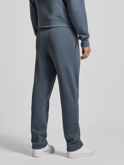 Mężczyznę model nosi Straight Fit Sweatpants mit Label-Stitching od CHAMPION z mieszanki bawełny, elastyczny pas, długość wewnętrzna 70 cm, kolor niebieskoszary, tekstura gładka, spodnie z prostymi nogawkami, widok całej sylwetki z tyłu.