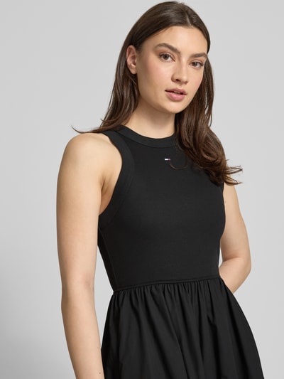 Frauenmodel trägt Midikleid aus reiner Baumwolle von Tommy Jeans, unifarben schwarz, A-Linie, Rundhals, ärmellos, Nahaufnahme Oberkörper.
